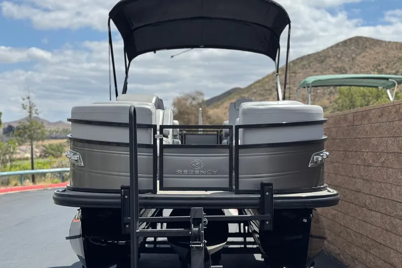 Slide: The Image of 2024 Regency 230 DL3 pontoon boat with canopy, parked near scenic mountains. - 2