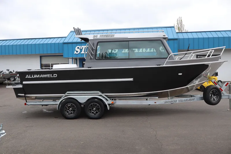 The Image of 2026 Alumaweld Horizon 24 boat on trailer, parked outside a blue-roofed building. - 1