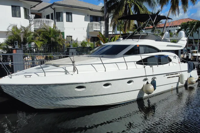 Slide: The Image of 1998 Azimut 52 yacht docked near waterfront homes, surrounded by tropical palm trees. - 62