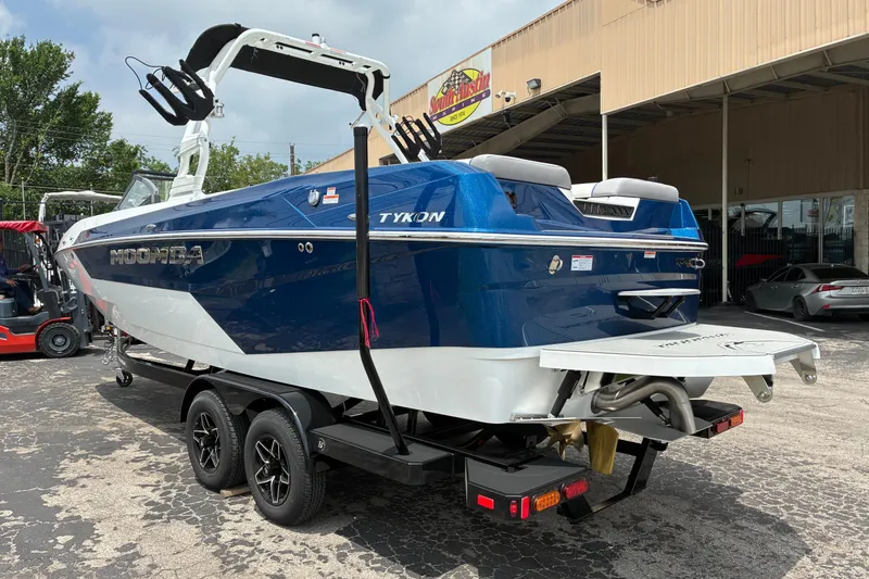 Slide: The Image of 2026 Moomba Tykon boat on trailer, blue and white design, parked outside a building. - 6