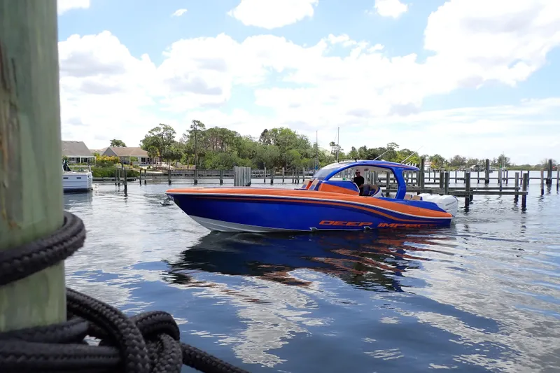 Slide: The Image of 2022 Deep Impact 369 Sport boat on calm water near a dock, under a partly cloudy sky. - 112