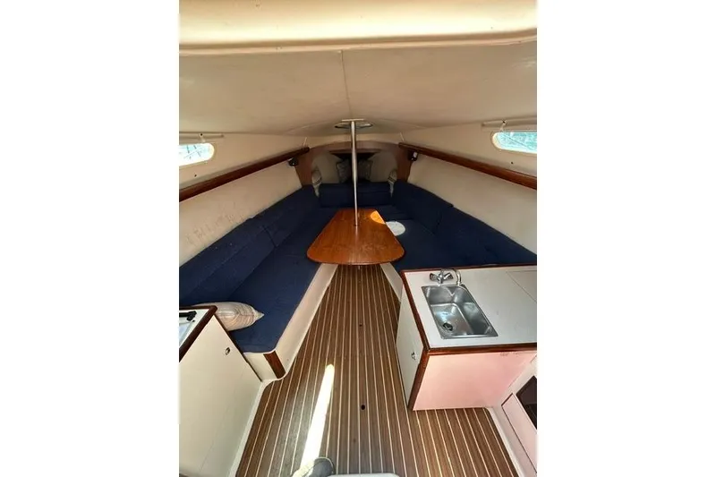 Slide: The Image of 2005 Hunter 27 sailboat interior with blue seating, wooden table, and compact kitchenette. - 19