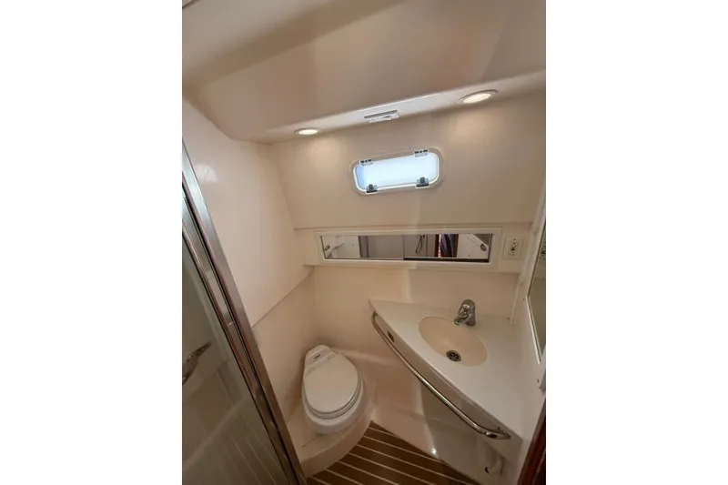 Slide: The Image of Compact bathroom in a 2003 Cabo 35 Express boat, featuring a toilet, sink, and mirror. - 26