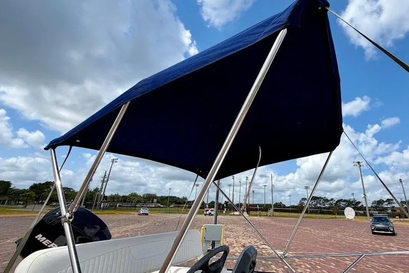 Slide: The Image of 2002 Boston Whaler 130 Sport with blue canopy, parked on brick pavement under cloudy sky. - 9