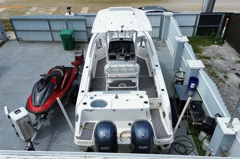 Slide: The Image of 2022 Robalo R242 Center Console boat with dual engines, parked beside a red jet ski. - 15