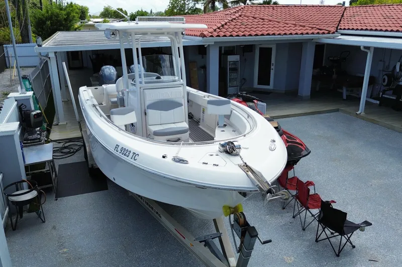 Slide: The Image of 2022 Robalo R242 Center Console boat parked in a driveway with red chairs nearby. - 9