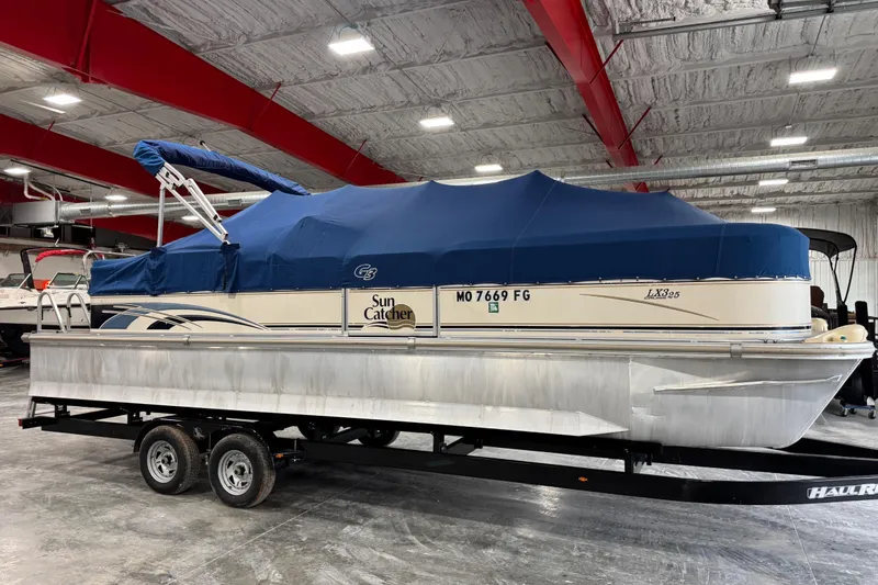Slide: The Image of 2006 G3 Sun Catcher pontoon boat with blue cover on trailer in indoor storage. - 11