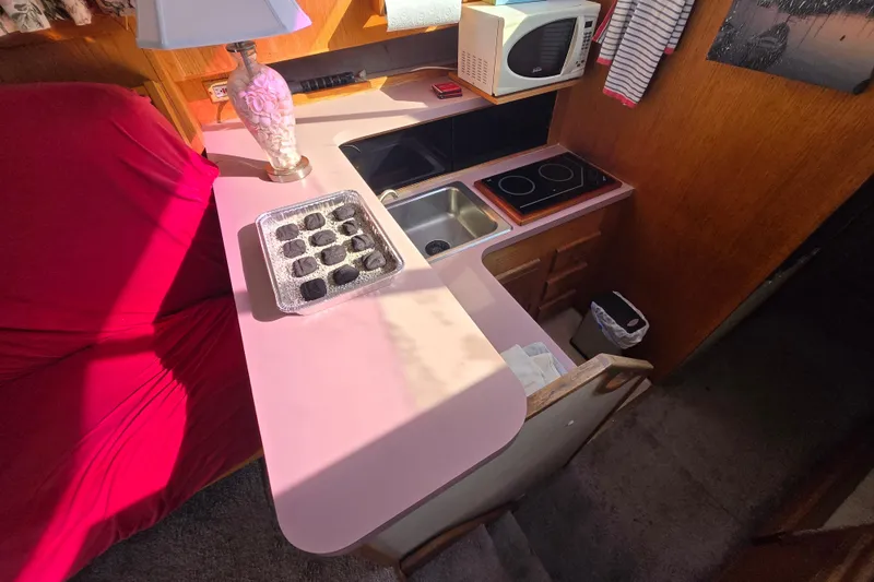 Slide: The Image of 1988 Silverton 34 Convertible interior with kitchenette, featuring sink, stove, microwave, and red sofa. - 9