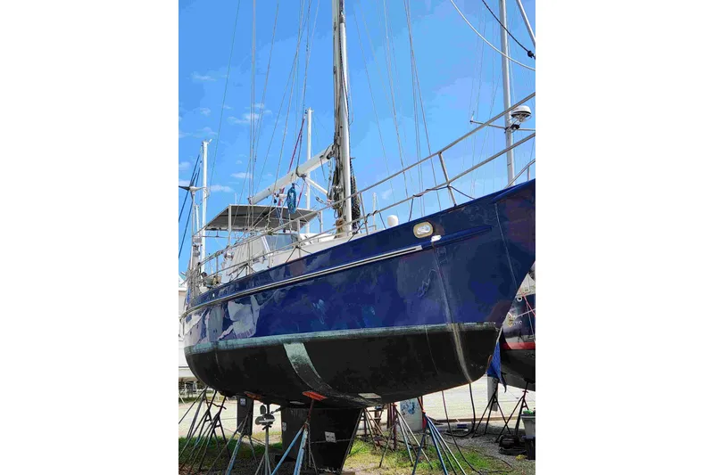 Slide: The Image of Sailboat on stands, Custom Bruce Roberts model, 2000, with blue hull under clear sky. - 12