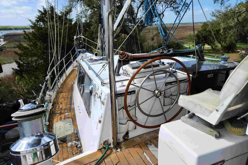 Slide: The Image of Sailboat deck with wooden wheel, Custom Bruce Roberts model, 2000, surrounded by lush greenery. - 16