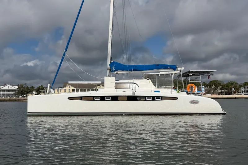 Slide: The Image of 2007 Dolphin 460 catamaran with blue sail, docked near waterfront homes under cloudy sky. - 8