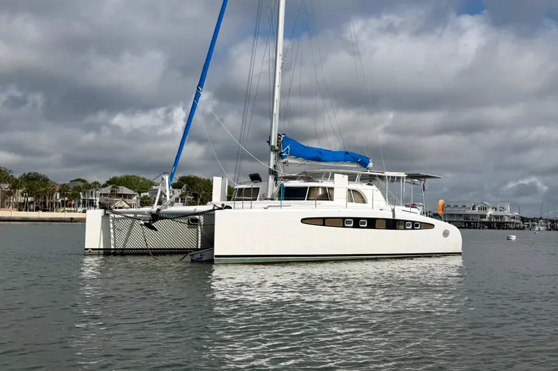 Slide: The Image of 2007 Dolphin 460 catamaran with blue sail, anchored in calm waters under cloudy skies. - 9