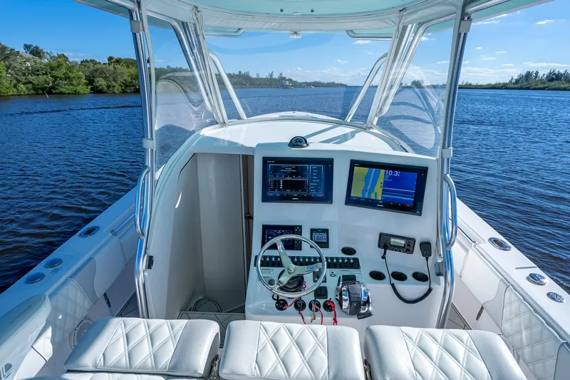 Slide: The Image of 2019 Contender 39 Fisharound boat cockpit with advanced navigation systems on a serene waterway. - 16