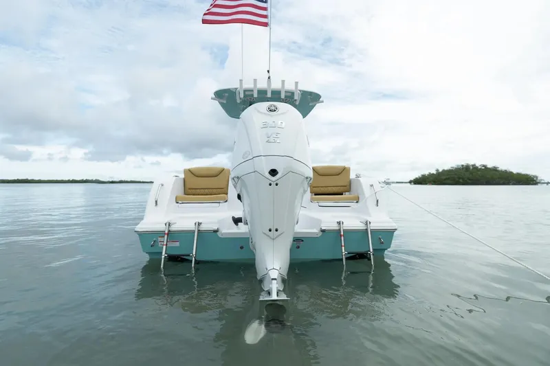 Slide: The Image of Manufacturer Provided Image: 2025 Sportsman Heritage 231 Center Console boat on calm water, rear view with American flag. - 2