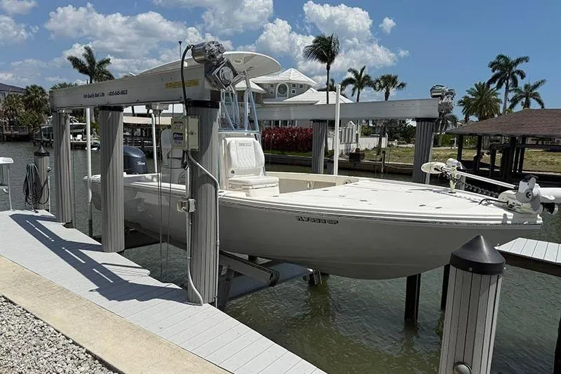 Slide: The Image of 2020 Pathfinder 2500 Hybrid boat on lift, docked by waterfront homes and palm trees. - 2