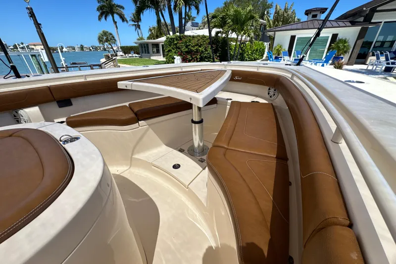 Slide: The Image of 2018 Scout 355 LXF boat interior with brown seating and table, docked near waterfront homes. - 33