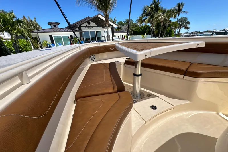 Slide: The Image of 2018 Scout 355 LXF boat interior with brown leather seating and table, surrounded by palm trees. - 34
