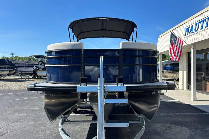Slide: The Image of 2026 Harris Cruiser 230 CWDH pontoon boat at dealership, front view with American flag. - 2