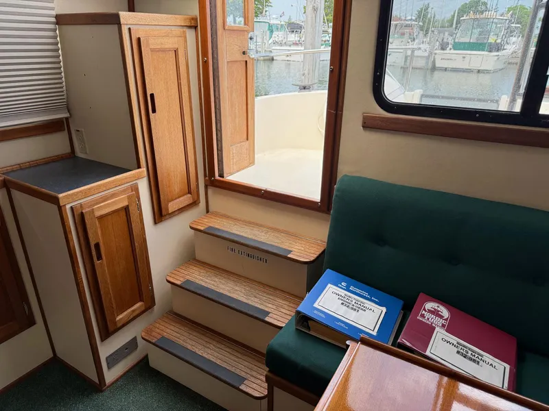Slide: The Image of Interior of a 1998 Nordic Tug Trawler with wooden cabinetry and manuals on a green seat. - 13