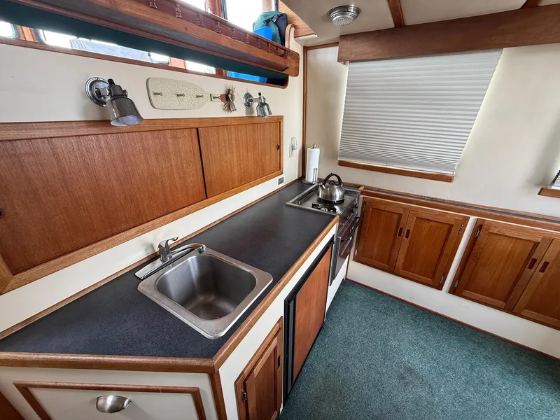 Slide: The Image of 1998 Nordic Tug Trawler kitchen with wooden cabinets, sink, and stove. - 14