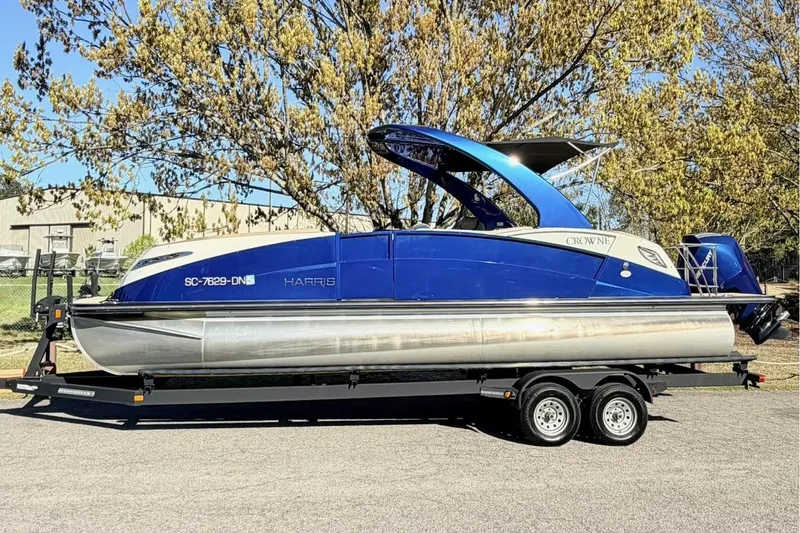 The Image of 2021 Harris Crowne SL 250 pontoon boat on trailer, parked near tree. - 0