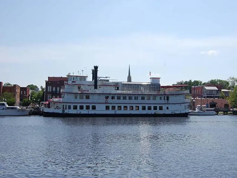 The Image of Custom 1985 Serodino Dinner Boat docked on a calm river, with cityscape background. - 0