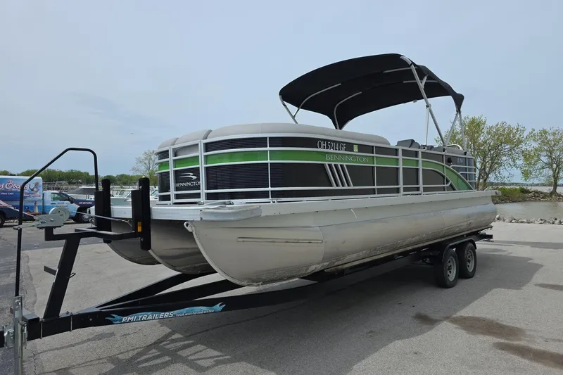 Slide: The Image of 2021 Bennington LX 24 Quad Bench pontoon boat on trailer, parked near water. - 2