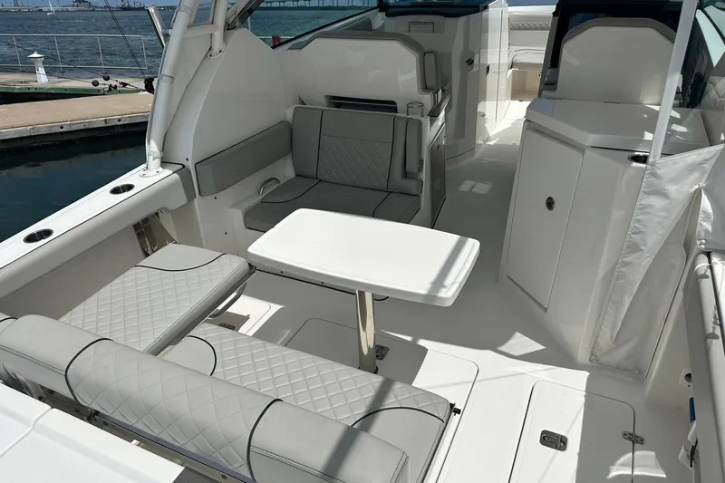 Slide: The Image of 2023 Pursuit DC 295 Dual Console boat interior with seating and table, docked by the water. - 17