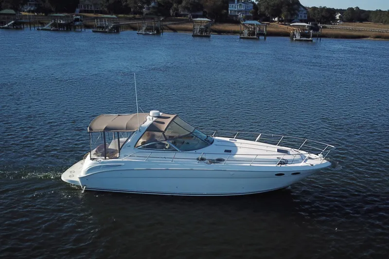The Image of 1999 Sea Ray 380 Sundancer cruising on a calm river near docks and houses. - 1