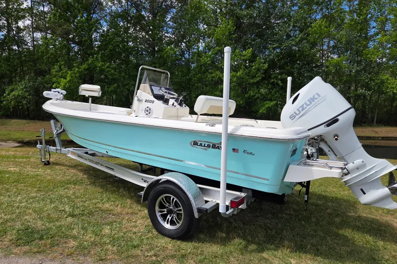 Slide: The Image of 2023 Bulls Bay 2000 boat with Suzuki engine on trailer, parked on grass. - 2