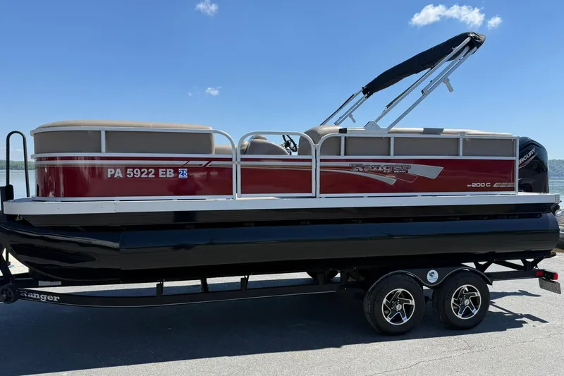 The Image of 2022 Ranger 200C pontoon boat on trailer, red and beige design, sunny day. - 1