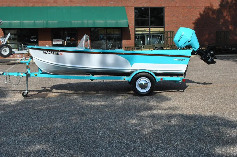 Slide: The Image of 2025 Starcraft 57 Ski Champ boat on trailer, parked outdoors, featuring a turquoise and white design. - 13