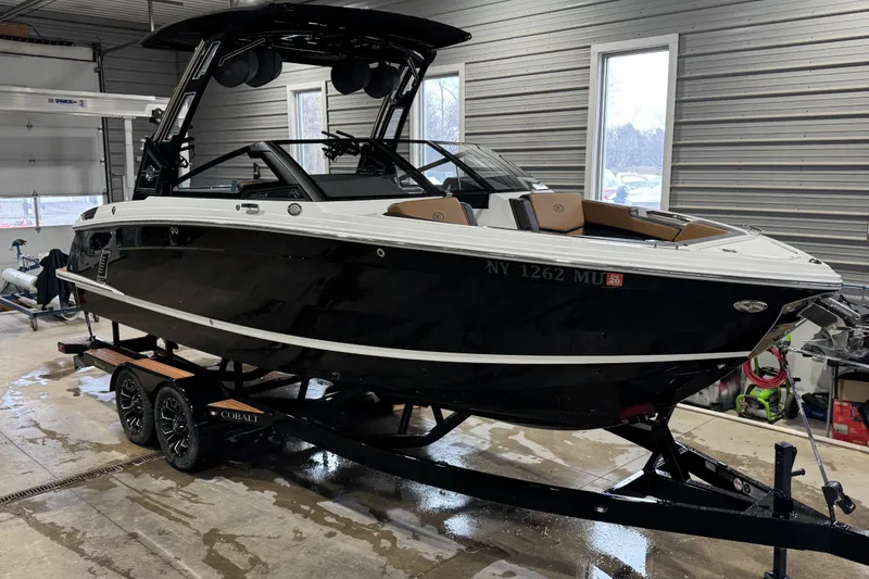 The Image of 2023 Cobalt R6 Surf boat in a garage, black and white exterior, on a trailer. - 1