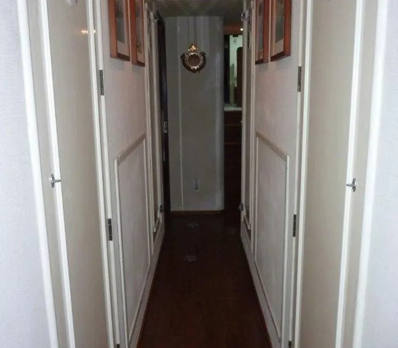 Slide: The Image of Narrow hallway inside a 1987 Hatteras Flybridge yacht, featuring wooden flooring and white doors. - 16