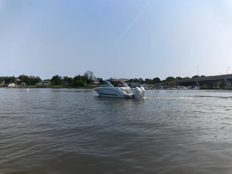 Slide: The Image of A 2027 Sea Ray SLX 310 Outboard cruising on a calm river, surrounded by trees and bridges. - 3
