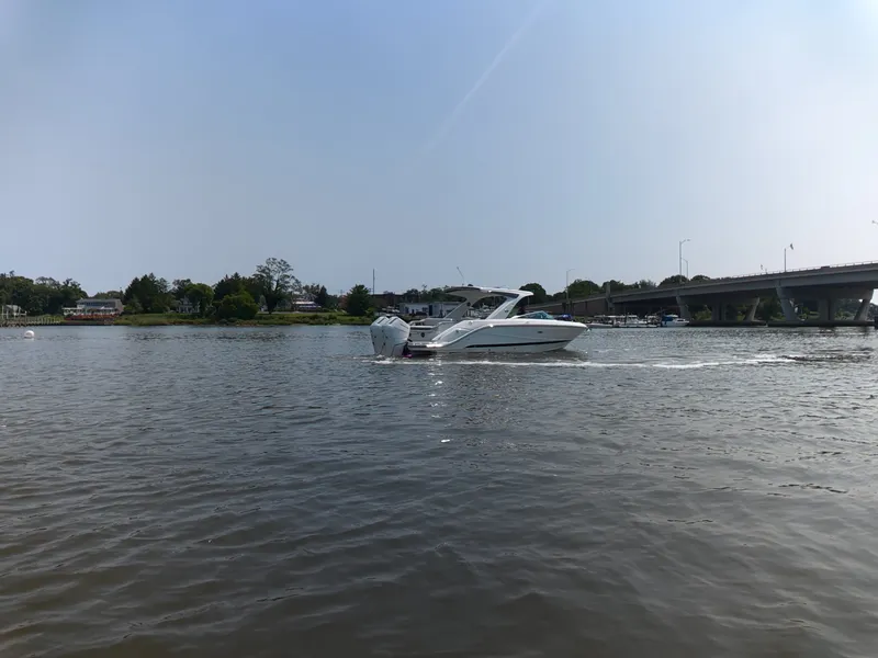 Slide: The Image of A 2027 Sea Ray SLX 310 Outboard cruising on a calm river under a bridge. - 9
