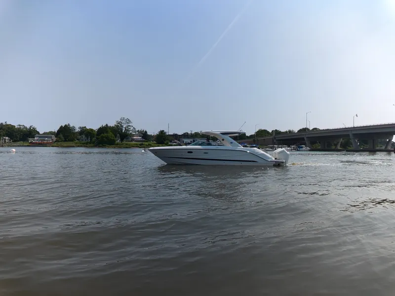 Slide: The Image of Sea Ray SLX 310 Outboard 2027 on calm water, near a bridge and shoreline. - 2