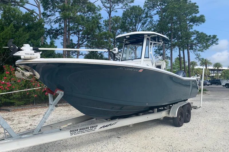 The Image of 2021 Tidewater 256 CC Adventure boat on trailer, surrounded by trees and parked on gravel. - 0