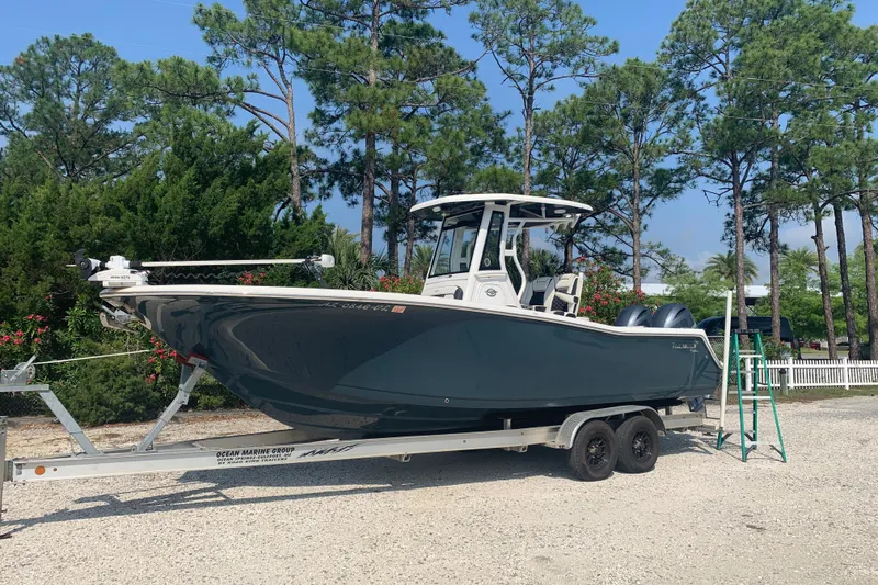 Slide: The Image of 2021 Tidewater 256 CC Adventure boat on trailer, surrounded by trees. - 2