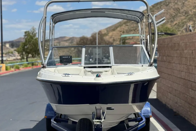 Slide: The Image of 2006 Bayliner 195 Bowrider boat on trailer, parked outdoors with scenic background. - 2
