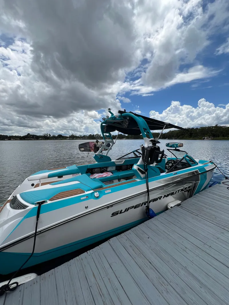 Slide: The Image of 2018 Nautique Super Air G23 boat docked on a lake under cloudy skies. - 0