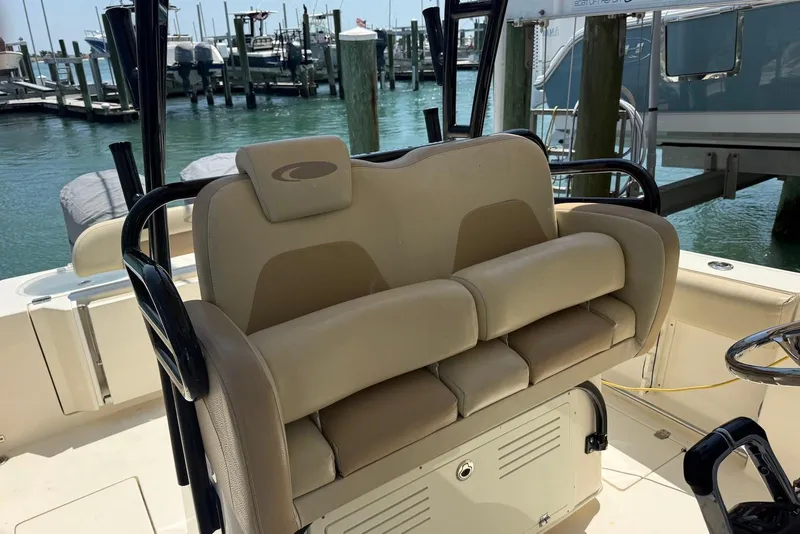Slide: The Image of 2015 Cobia 296 Center Console boat interior with beige seating at a marina. - 11