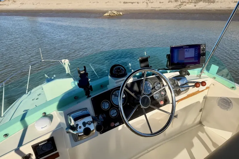 Slide: The Image of 1981 Bertram 28 Flybridge Cruiser helm with steering wheel and navigation equipment on calm water. - 12