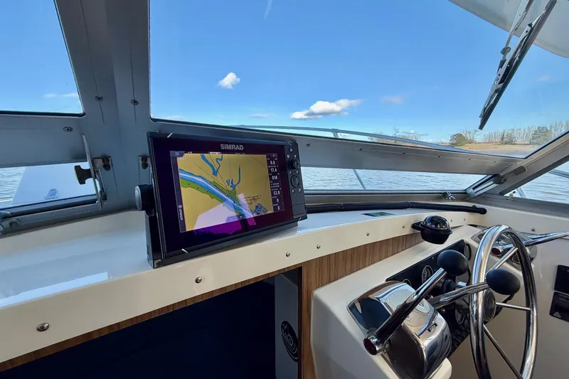 Slide: The Image of 1981 Bertram 28 Flybridge Cruiser helm with Simrad navigation system, overlooking calm waters. - 19