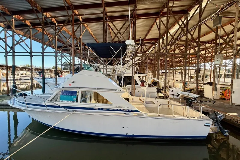Slide: The Image of 1981 Bertram 28 Flybridge Cruiser docked in a marina under a covered structure. - 25