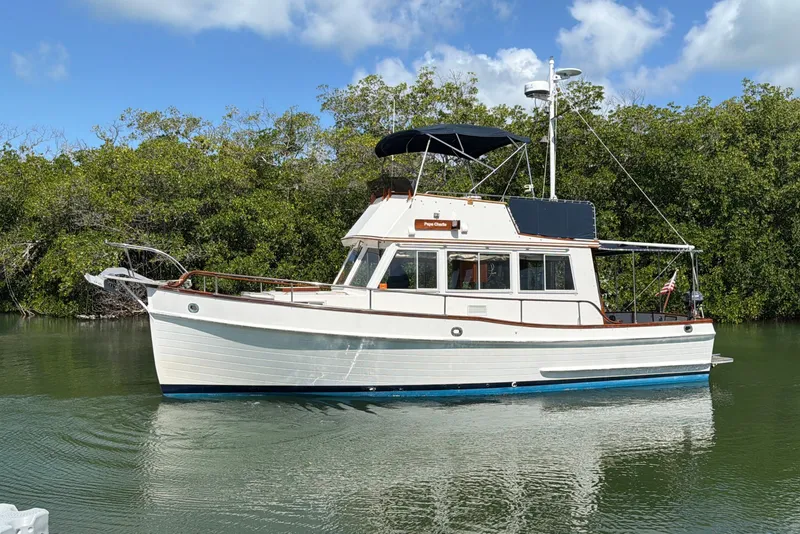 The Image of 1983 Grand Banks 32 Sedan boat on calm water, surrounded by lush greenery. - 0