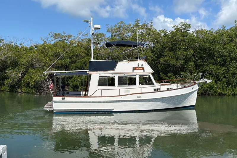 Slide: The Image of 1983 Grand Banks 32 Sedan boat on calm water, surrounded by lush greenery. - 11