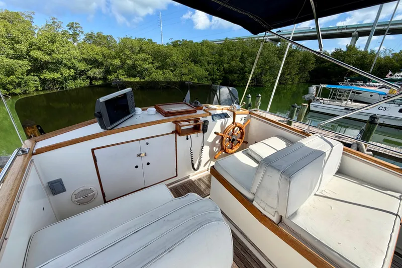 Slide: The Image of 1983 Grand Banks 32 Sedan boat interior with steering wheel and seating, docked near lush greenery. - 12