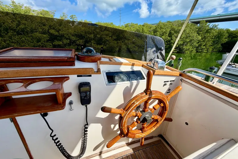 Slide: The Image of 1983 Grand Banks 32 Sedan helm with wooden wheel, radio, and lush green backdrop. - 14