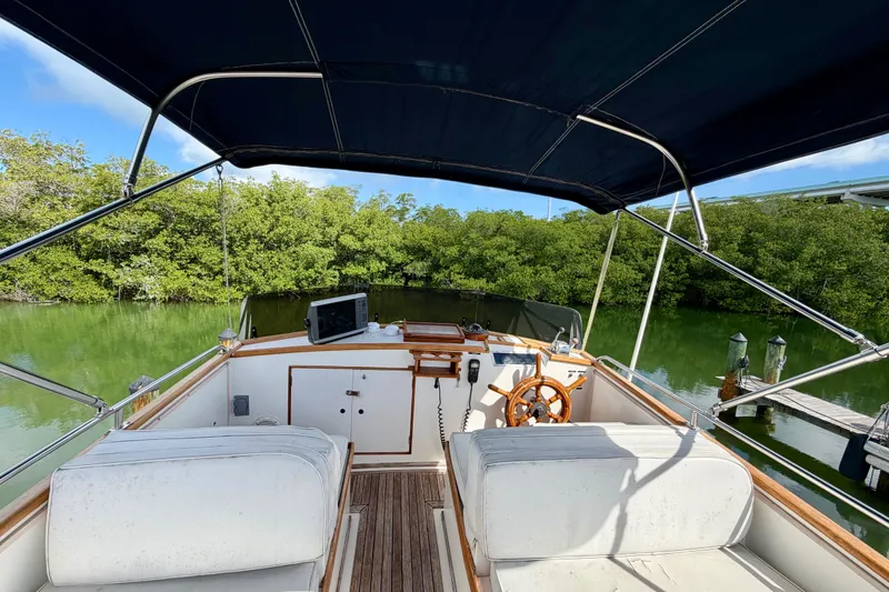 Slide: The Image of 1983 Grand Banks 32 Sedan boat interior with canopy, steering wheel, and lush greenery backdrop. - 2